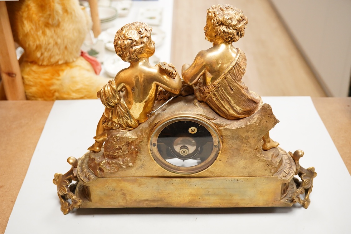 A Louis XV style figural brass mantel clock striking on a bell, with enamel dial and inset plaques, surmounted with two figures, with pendulum, no key, 42cm wide